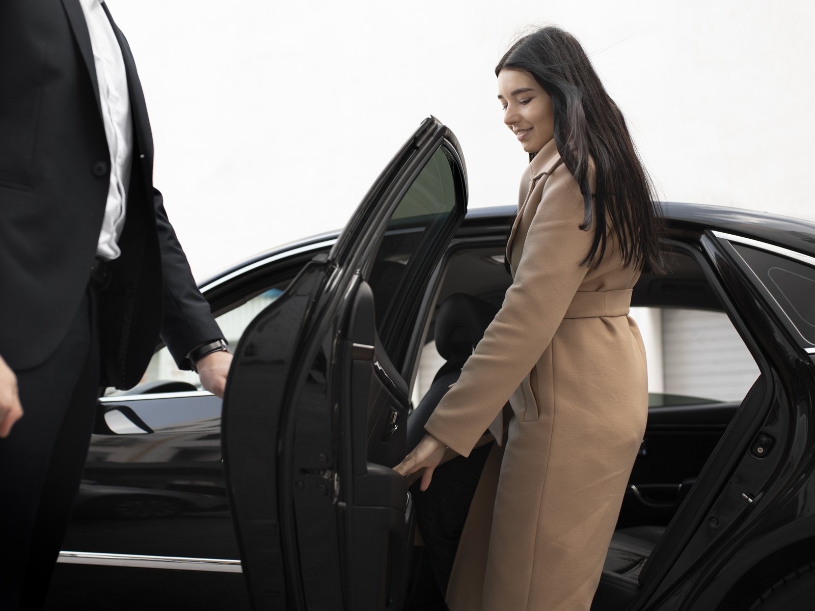 Chauffeur ouvrant la portière d'une berline noire à une cliente
